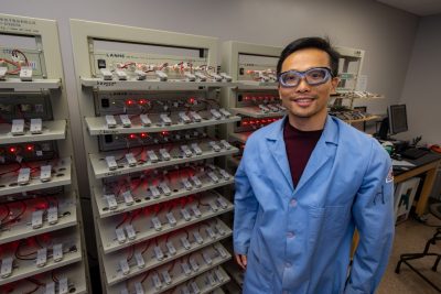 Man wearing lab goggles stands in front of battery display.